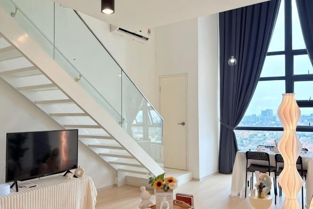 A modern living room with a staircase, a flat-screen TV, a dining area with a table and chairs, and a large window with curtains.