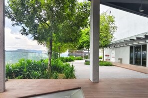 An outdoor area with a wooden deck, a pathway, and a building with a glass facade. - Urban Loft: MRT Convenience, KLCC Nearby @ Eko Cheras (Kuala Lumpur)
