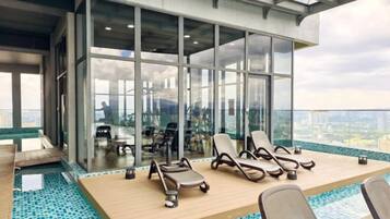 A modern indoor pool area with lounge chairs and a glass wall offering a city view.