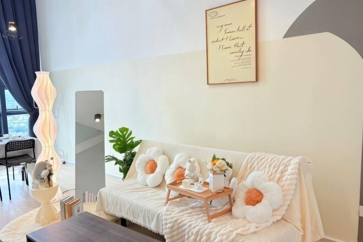 A modern hotel room with a sofa, a bedside table, a lamp, and a large window.
