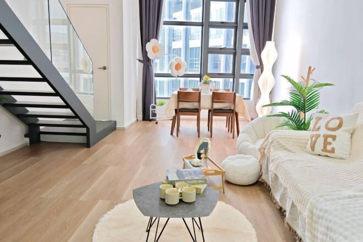 A modern living room with a staircase, a dining area with a table and chairs, and a cozy seating area with a sofa and a decorative pillow.