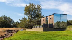 A modern, single-story building with a large glass facade, surrounded by a well-maintained lawn and trees. - RT Creekside Glass Retreat | Cowboy Pool/Hot Tub (Round Top)