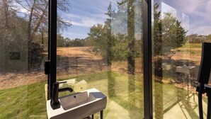 A bathroom with a sink and a window overlooking a dirt path and trees. - RT Creekside Glass Retreat | Cowboy Pool/Hot Tub (Round Top)
