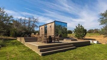 A modern outdoor deck with a wooden structure and glass enclosure, surrounded by a well-maintained lawn and trees.