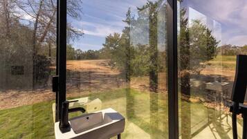 A bathroom with a sink and a window overlooking a dirt path and trees.