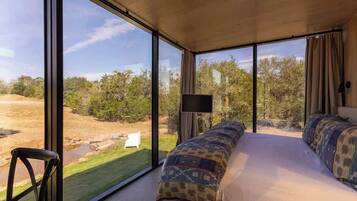 A bedroom with a large window, a bed, a chair, and a TV.