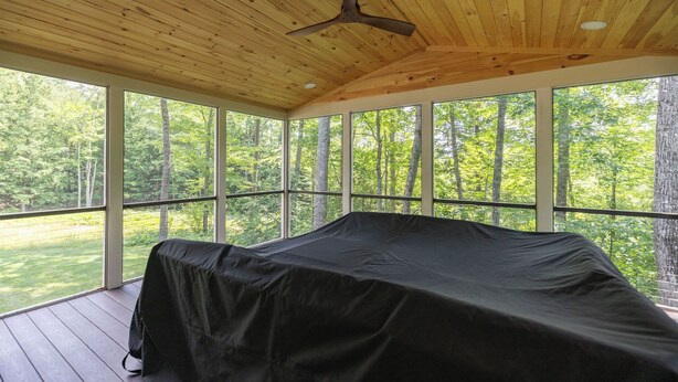 A covered outdoor deck with a ceiling fan, large windows, and a black outdoor seating area.