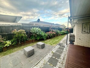 A backyard with a paved patio, outdoor furniture, a wooden deck, and a variety of plants.