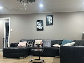 Un salon moderne avec un canapé en cuir noir, une petite table ronde et deux œuvres d’art florales accrochées au mur.
