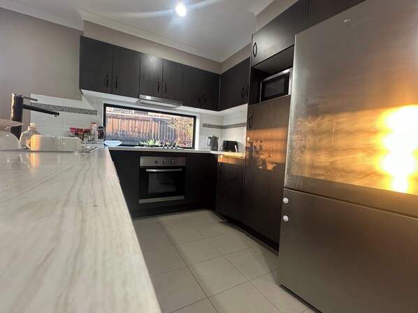 A modern kitchen with dark cabinets, a stainless steel refrigerator, and a window overlooking a wooden fence.