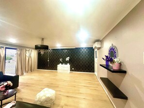 A spacious room with a wooden floor, a black patterned wall, a white dresser, a black chair, and a small white ottoman.
