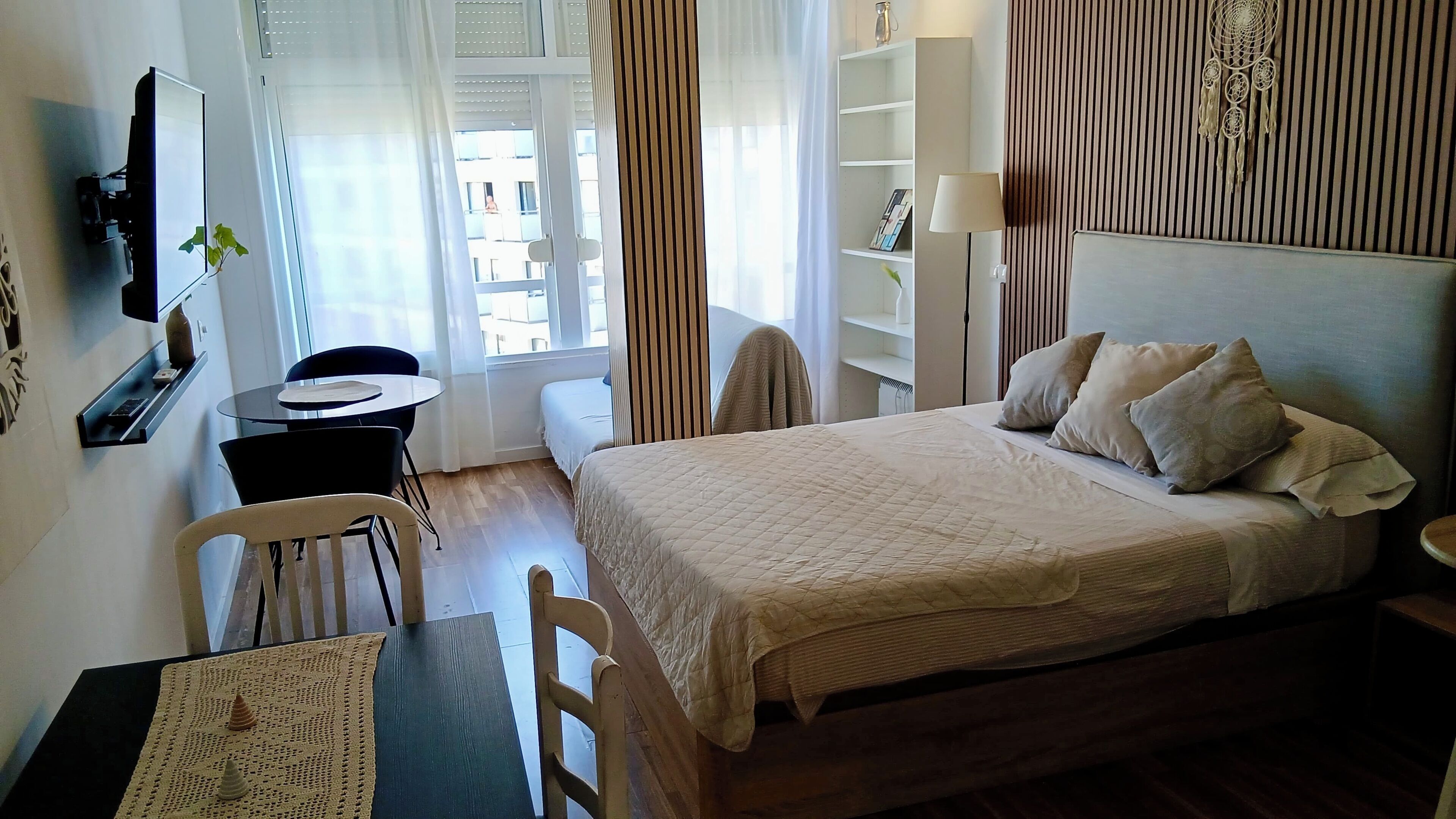 Een hotelkamer met een bed, een bureau met stoel, een televisie, een raam met gordijnen en een bedlamp.