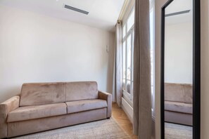 A room with a beige sofa, a large window, and a mirror.