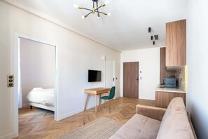 A modern living room with a sofa, a desk, a TV, and a kitchen area.
