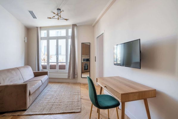 A modern living room with a sofa, a wooden desk, a TV, and a large window with curtains.