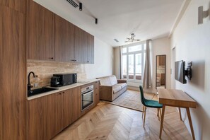 A modern kitchen with wooden cabinets, a built-in oven, and a coffee maker. There is a dining area with a wooden table and chairs.