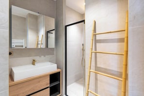 A modern bathroom with a white sink, mirror, and a bamboo shower ladder.