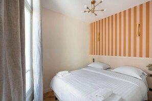 A hotel room with a large bed, a window with curtains, a striped wall, and a modern ceiling light fixture.