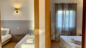 A hotel room with two beds, a bedside table, a lamp, and a window with curtains. - Ground floor 2 (Propriano)