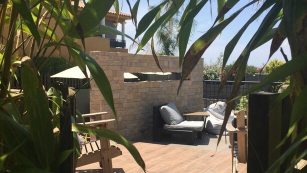 An outdoor patio area with a brick wall, a wooden deck, and a seating area with a lounge chair and a small table. - Ground floor 2 (Propriano)