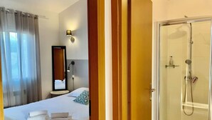 A hotel room with a bed, a bathroom with a glass shower, and a mirror on the wall. - Ground floor 2 (Propriano)