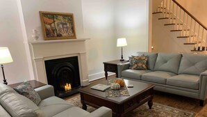 A living room with a fireplace, a sofa, a coffee table, and a staircase. - Madison Manor by the River | Hot Tub, Game Rm | 5 BRs, 4½ Bath, Sleeps 16 (Madison)