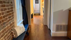 A hallway with a bench, a window with curtains, a door, and a wall with a clock. - Madison Manor by the River | Hot Tub, Game Rm | 5 BRs, 4½ Bath, Sleeps 16 (Madison)