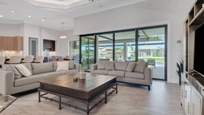 Amplia sala de estar con un sofá modular grande, una mesa de centro de madera y vistas al exterior a través de puertas correderas de vidrio.