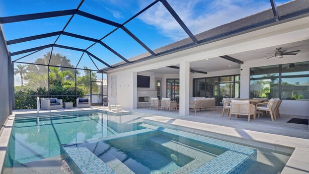 Una piscina interior moderna con paredes de vidrio, una terraza con mobiliario exterior y vistas despejadas de la vegetación circundante.