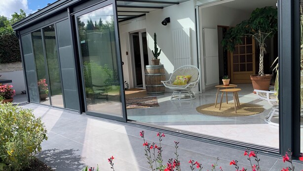 Een modern huis met een serre, een witte stoel met kussen en een potplant.