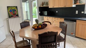 Een eethoek met een tafel voor vier personen, omringd door houten stoelen. Op de tafel staat een fruitschaal, en erboven een zwarte magnetron. De kamer heeft houten kastjes en een glazen deur die naar buiten leidt.