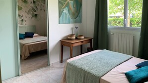 Een slaapkamer met een bed, een klein tafeltje met manden, een schilderij en een raam met gordijnen.