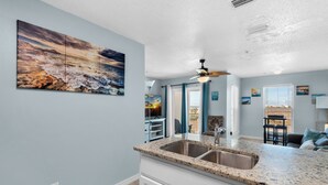 Una cocina con encimera de granito, pileta doble y ventilador de techo.