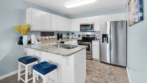 Una cocina moderna con armarios blancos, encimera de granito, electrodomésticos de acero inoxidable y taburetes de bar azules.