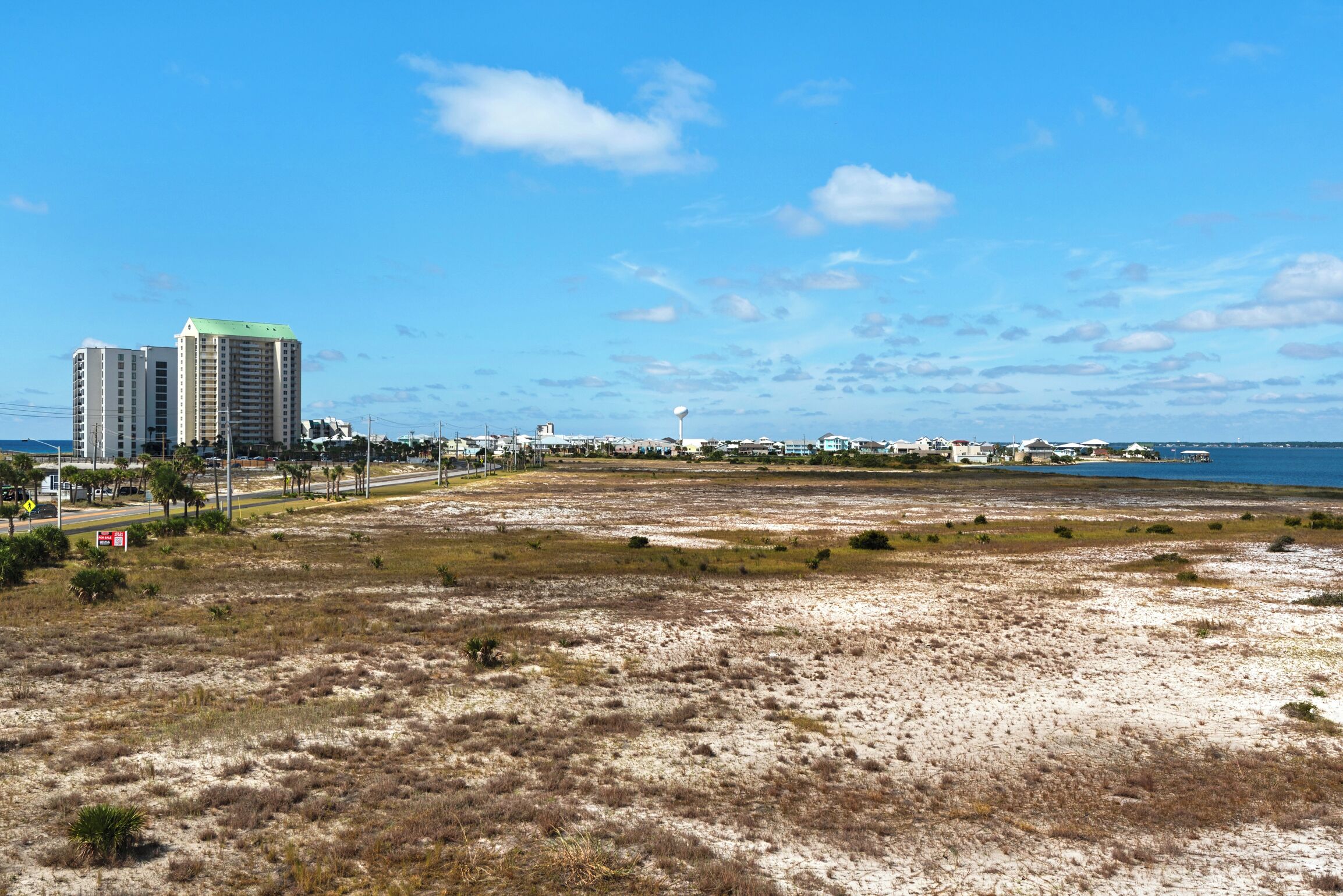 A coastal area with buildings, a beach, and a clear sky.