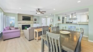 A modern living room with a fireplace, a dining area with a wooden table and chairs, and a kitchen with white cabinets and stainless steel appliances. - Steps to sand and surf, Parking in garage, Patio (Newport Beach)