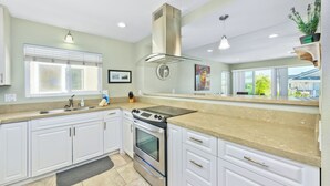 A modern kitchen with white cabinets, a stainless steel stove, and a large window providing natural light. - Steps to sand and surf, Parking in garage, Patio (Newport Beach)