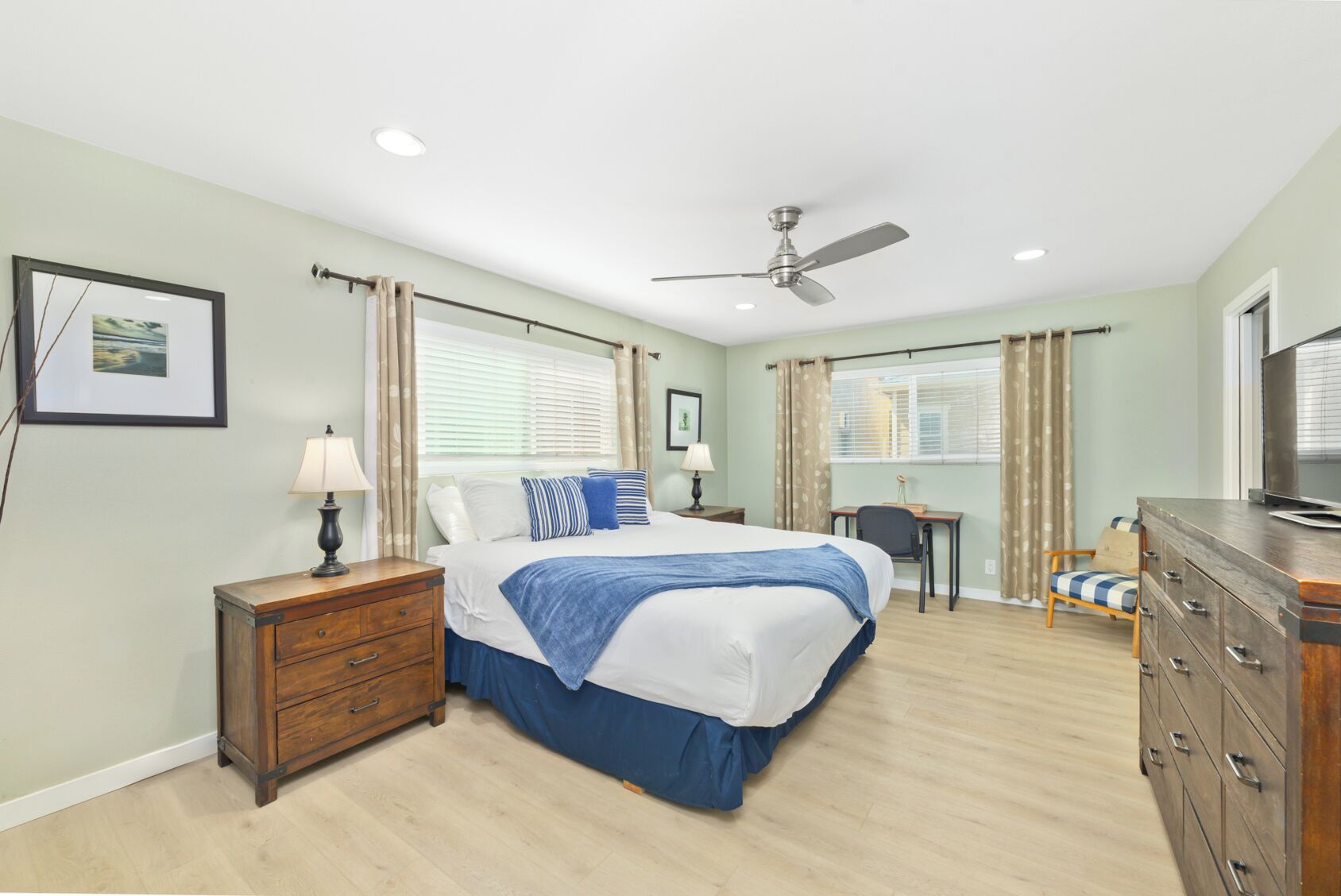 A bedroom with a bed, a desk, a dresser, and a ceiling fan.