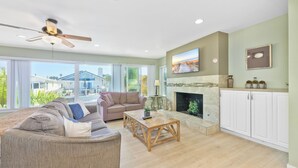 A spacious living room with a fireplace, a ceiling fan, and a large window offering a view of the outside. - Steps to sand and surf, Parking in garage, Patio (Newport Beach)
