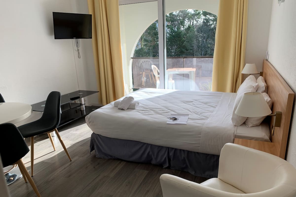 A hotel room with a bed, a desk, a chair, a TV, and a window with curtains.