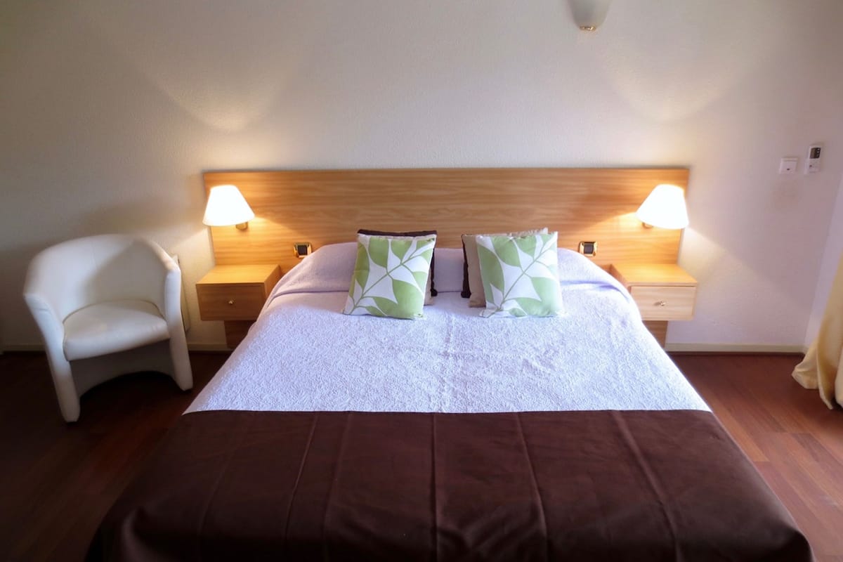 A neatly made bed with a brown bedspread, two pillows with leaf patterns, and two bedside lamps on wooden nightstands.