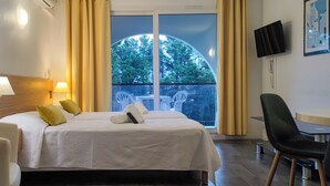 Ein Hotelzimmer mit einem Bett, einem Schreibtisch, einem Sessel, einem Fernseher und einem Fenster mit Vorhängen.