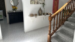 Um corredor com um console branco, um espelho e uma estátua de Buda. Uma escada com balaústres de madeira leva a um patamar.
