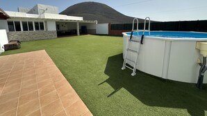 Um quintal com grama sintética, piscina e área de varanda coberta.