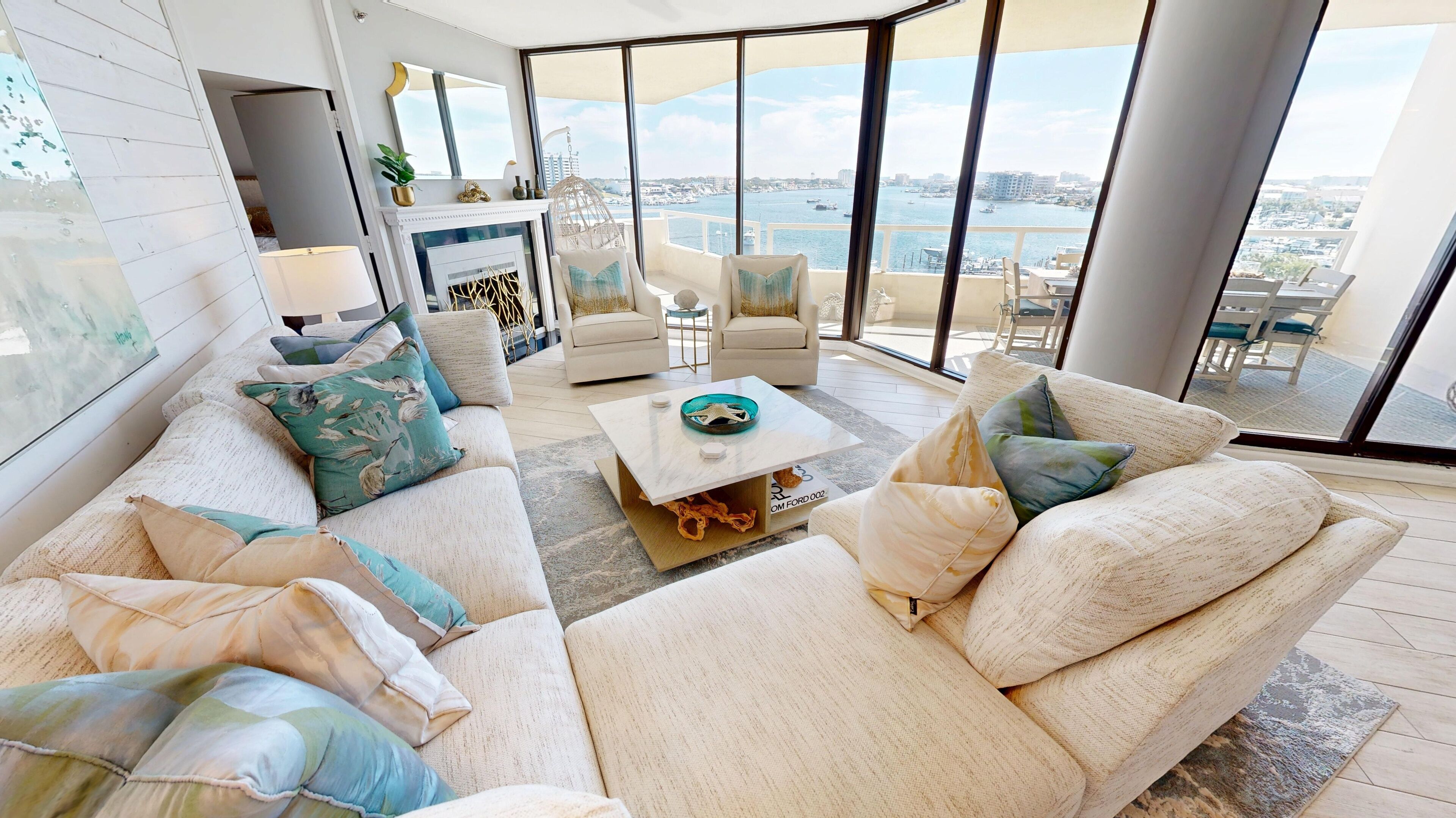 A modern living room with a sofa set, a coffee table, and a view of the water and cityscape.