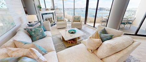 A modern living room with a sofa set, a coffee table, and a view of the water and cityscape.