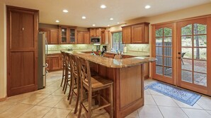 A spacious kitchen with wooden cabinets, a large island with bar stools, a refrigerator, and a microwave. - 4 Tan Oak Lane 5 Bedroom Home (Bend)