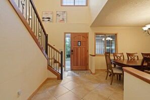 Uma área de refeições com uma mesa e cadeiras de madeira, uma escada com corrimão de madeira e uma porta que dá para o exterior.
