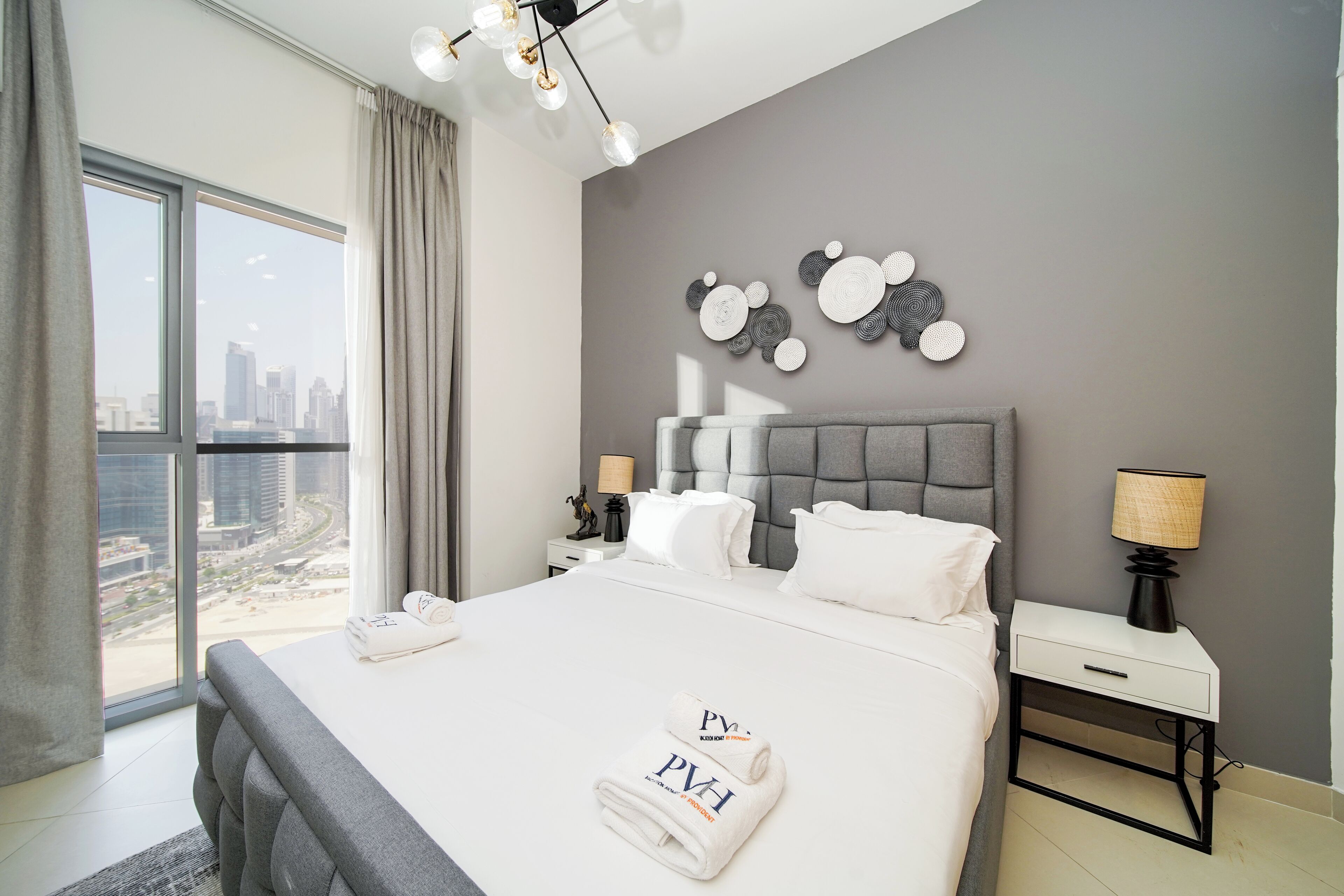 A modern hotel room with a large bed, a city view, and a unique wall art piece.