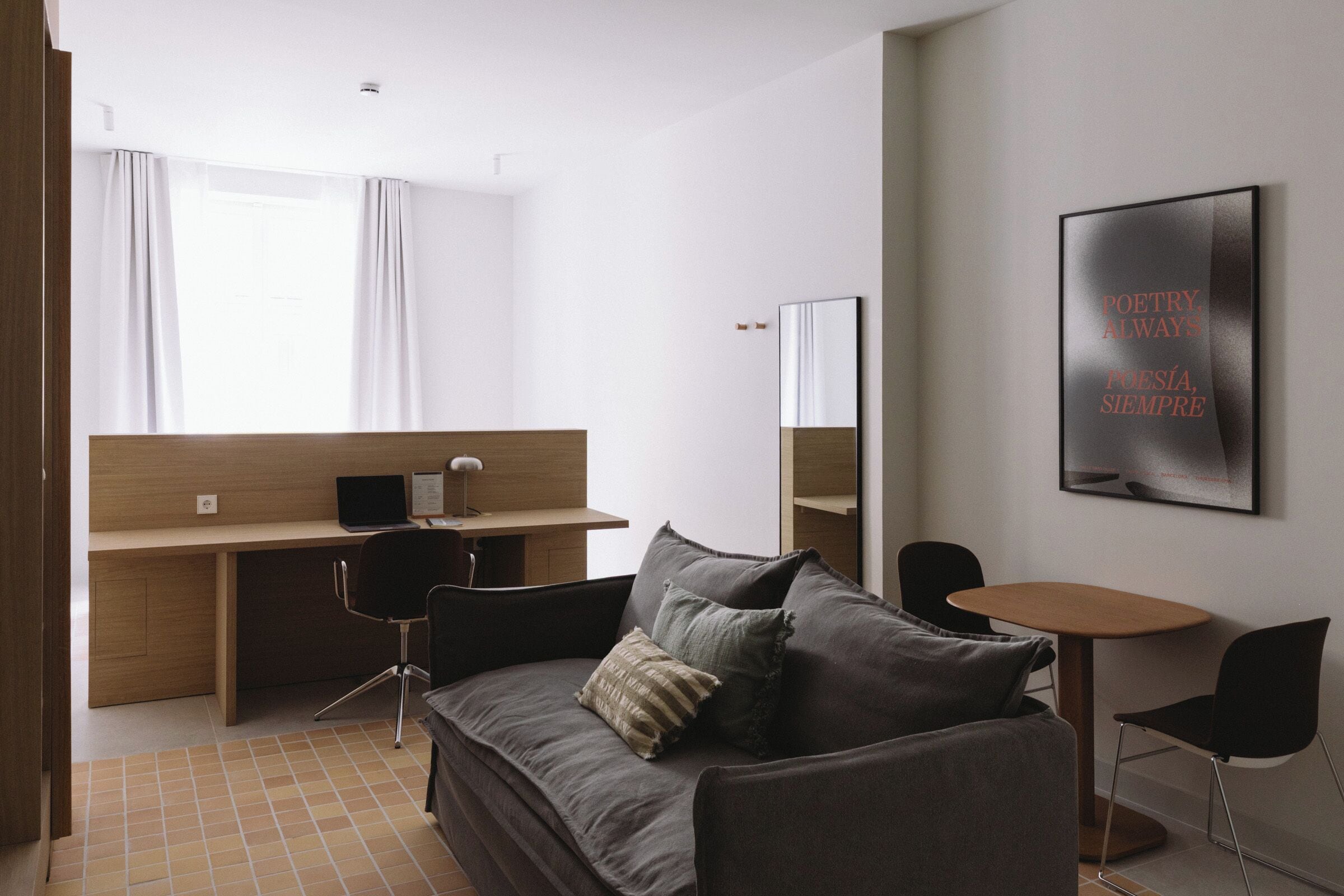 Ein modernes Hotelzimmer mit einer Couch, einem kleinen Tisch, einem Schreibtisch mit Stuhl, einem Spiegel und einem gerahmten Zitat an der Wand.
